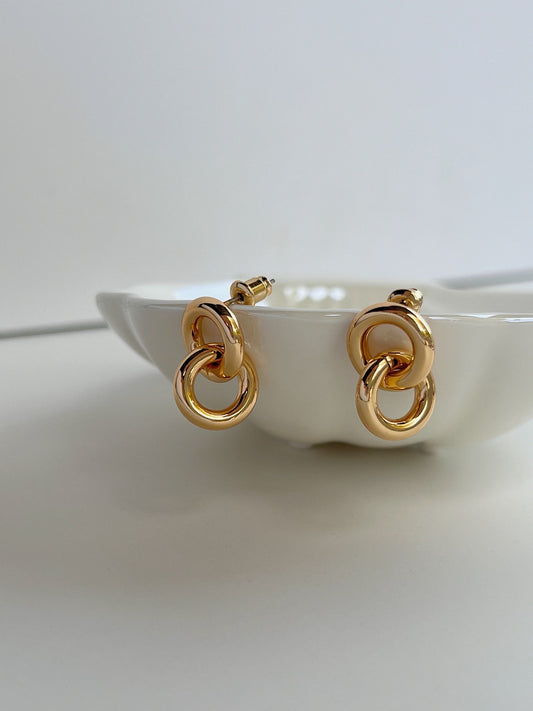 Elegant gold double hoop earrings with interlocking design on white ceramic dish.