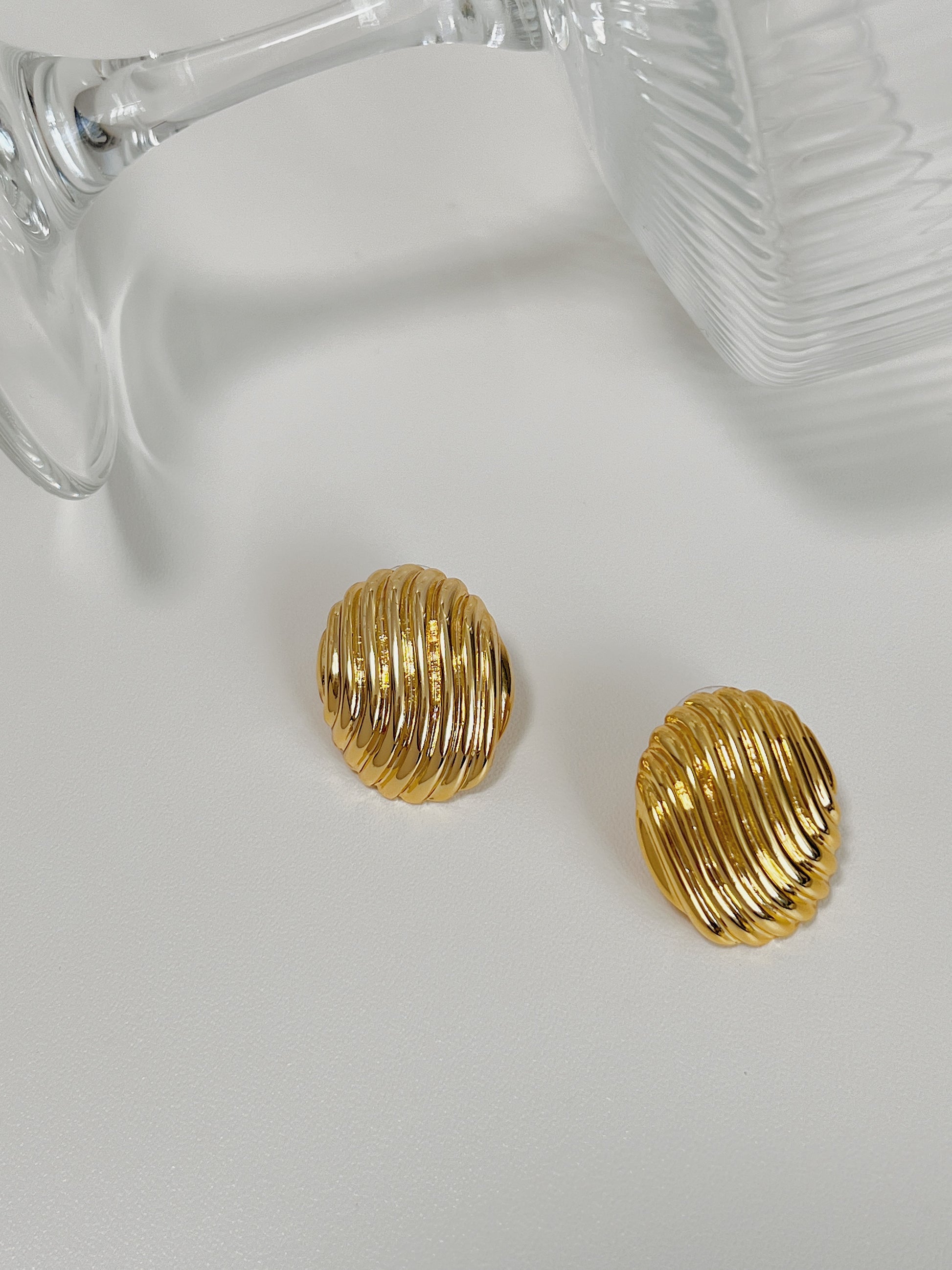 High-quality gold ribbed oval earrings showcasing beside a cocktail glass.