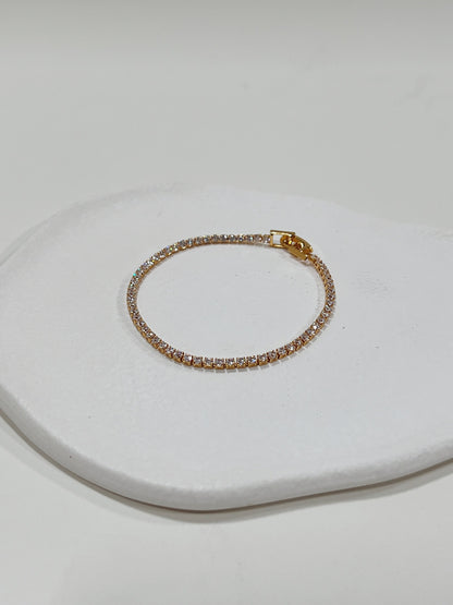 Shimmering diamond tennis bracelet in gold, resting on a white ceramic plate.