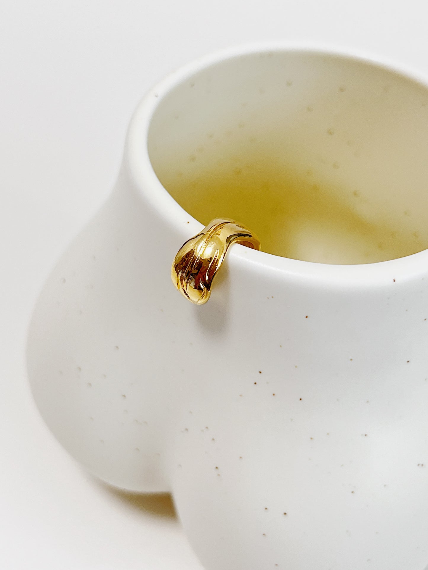 Gold ribbed ear cuff on white ceramic cup on a white background
