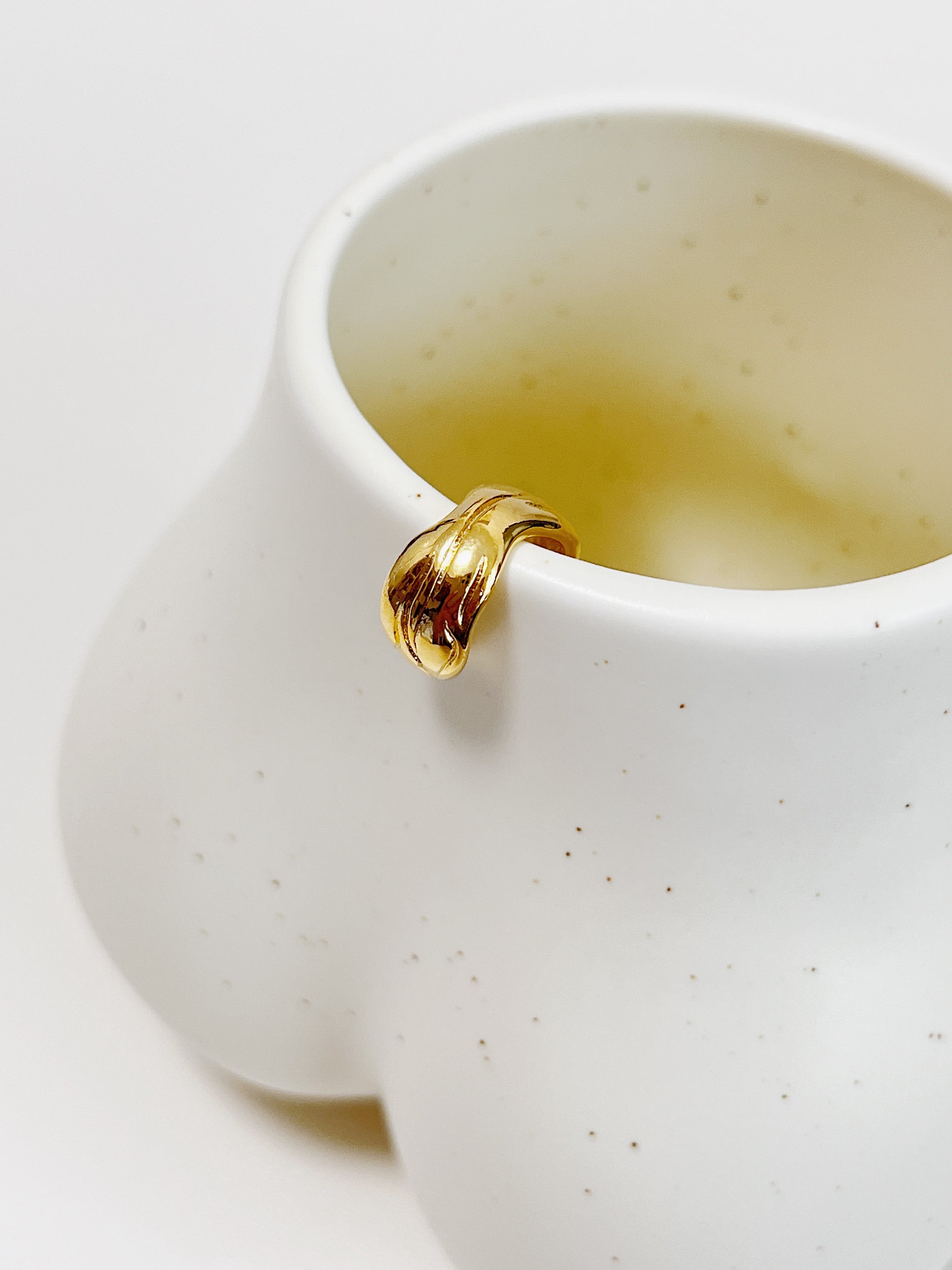 Gold ribbed ear cuff on white ceramic cup on a white background