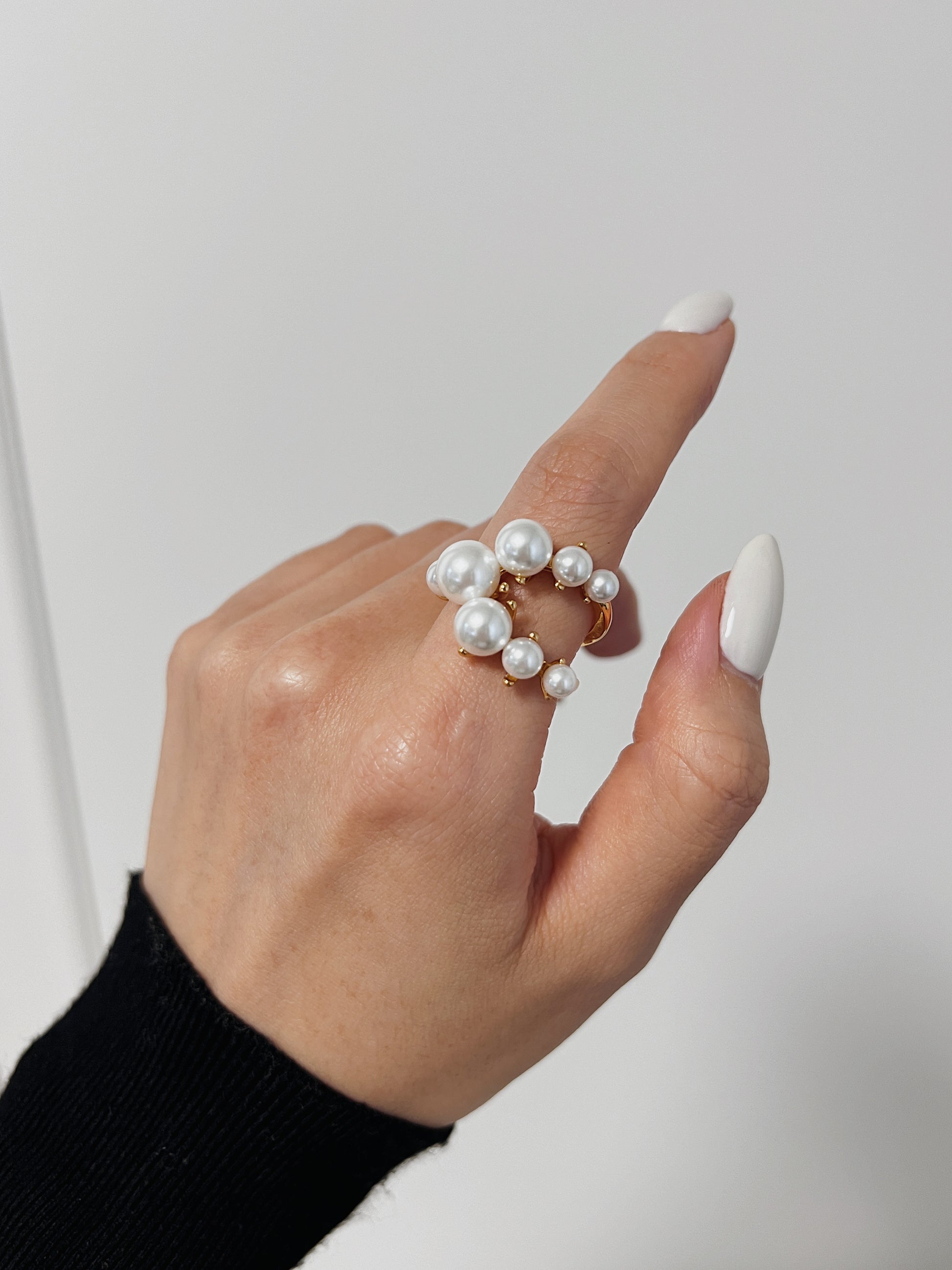 Hand wearing a pearl ring on a plain background