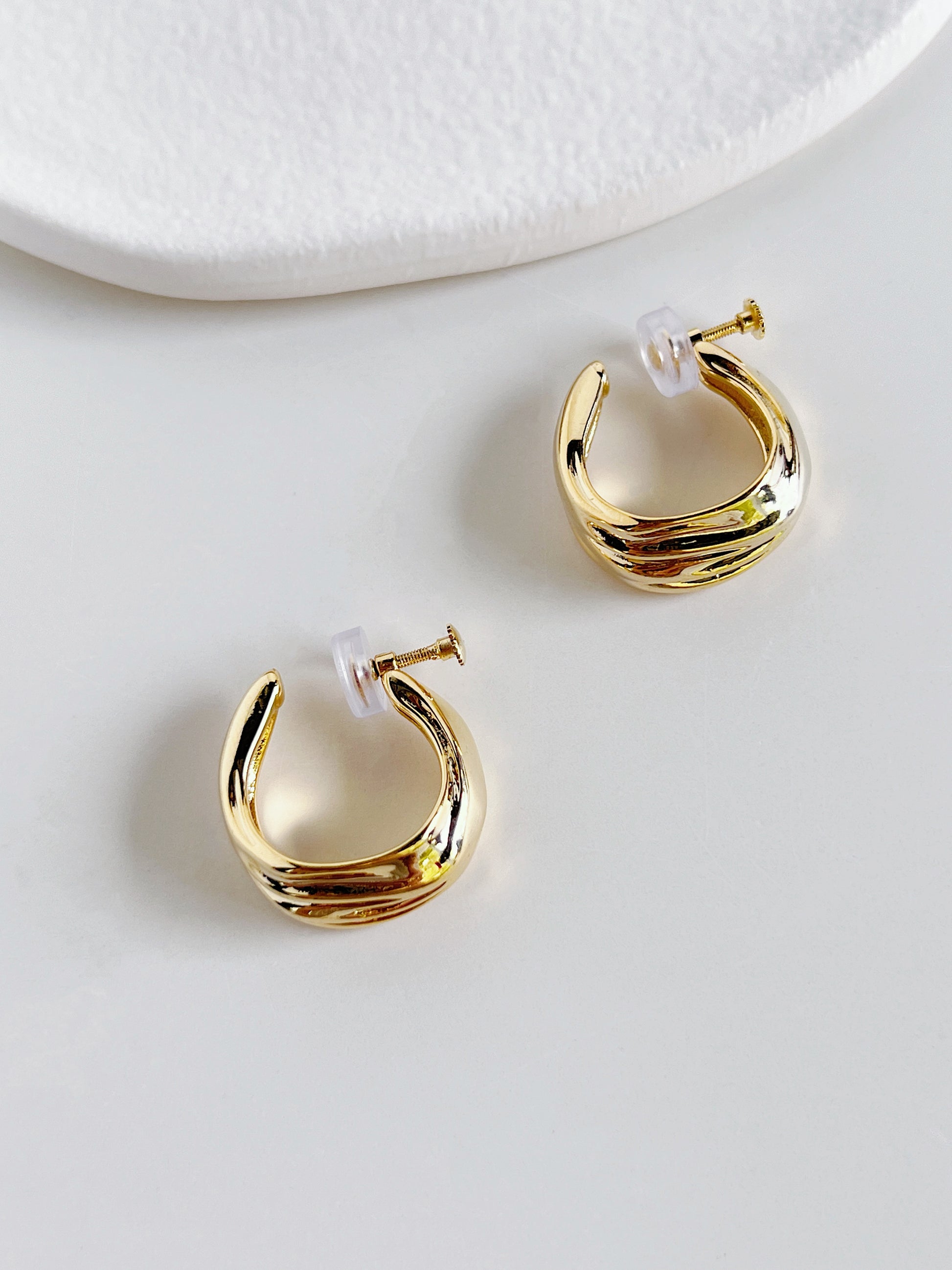 Gold screw back clip on hoop earrings on a white surface
