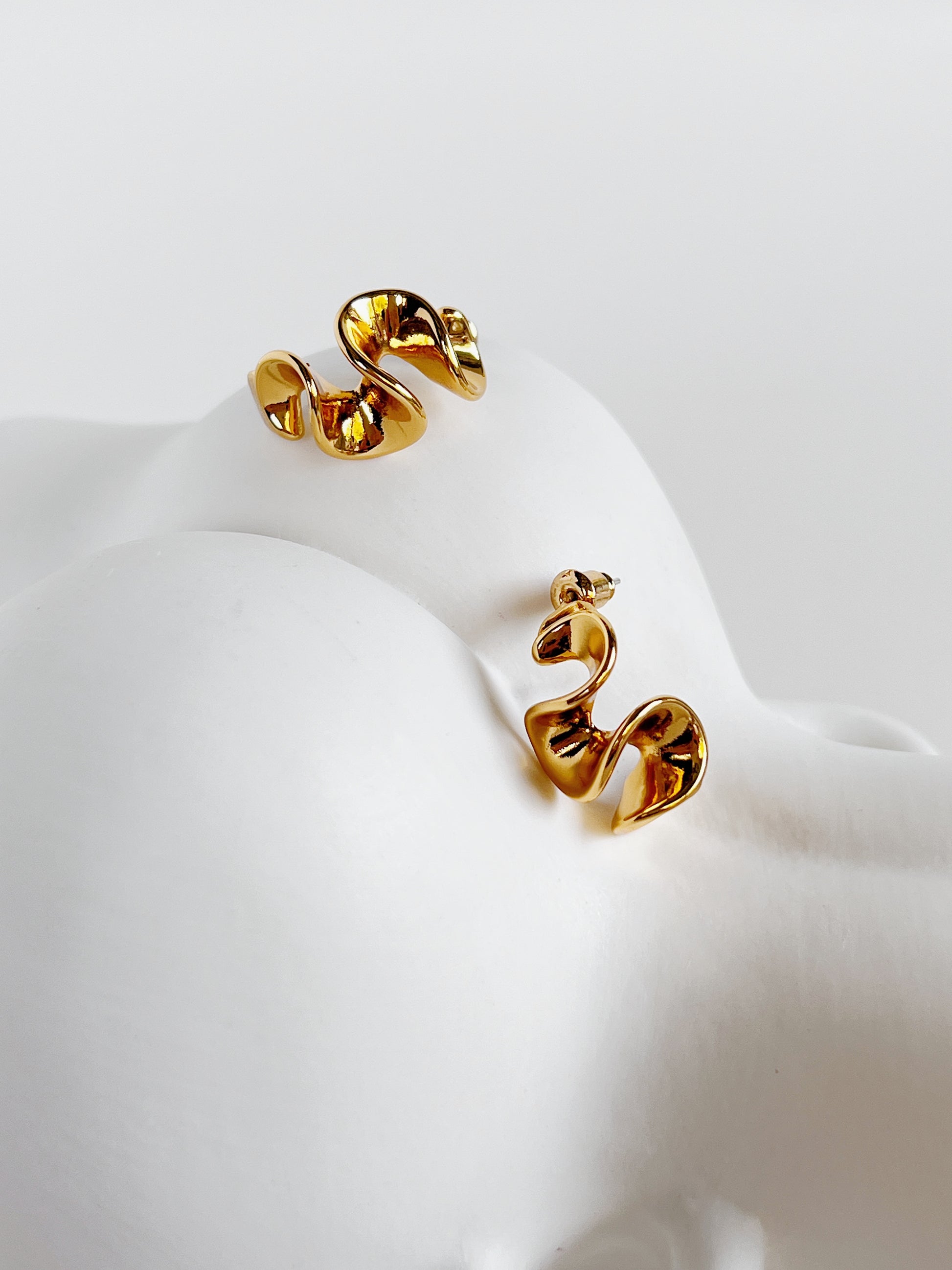 Pair of gold wavy earrings on a white ceramic vase