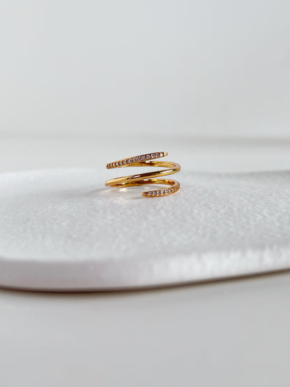Gold spiral ring with embedded stones on a white surface