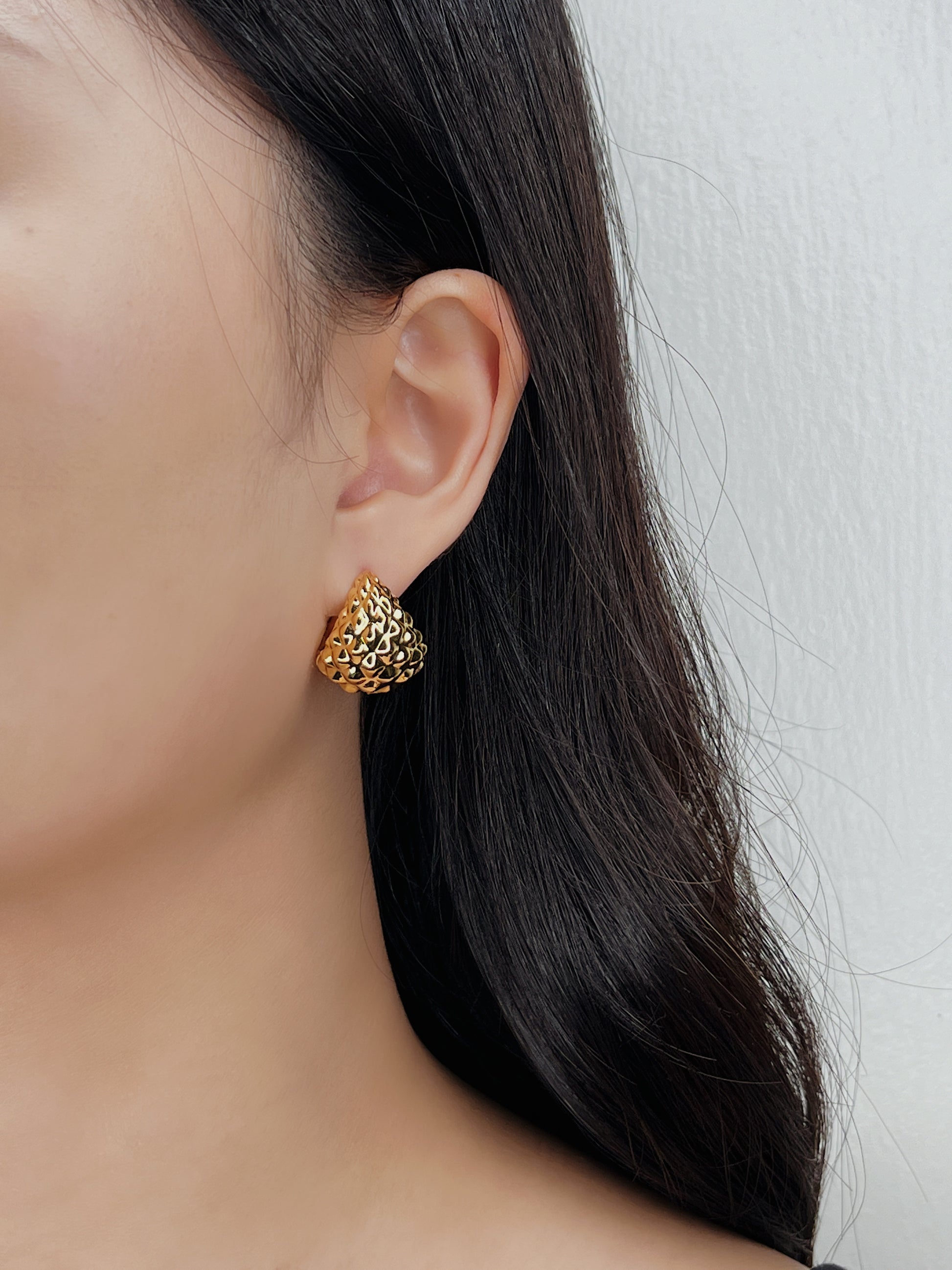 Gold earring worn by a person with dark hair against a neutral background