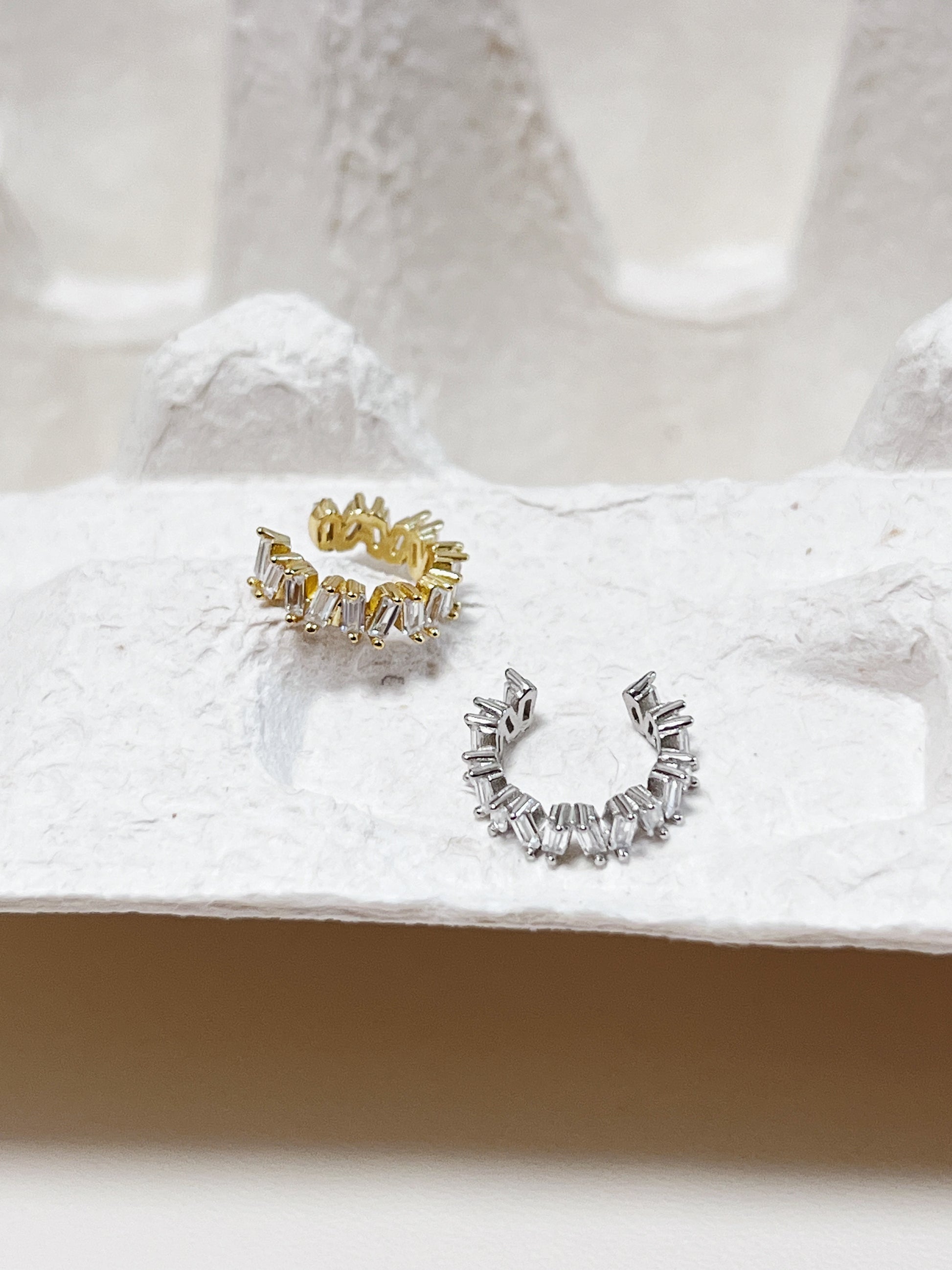 Gold and silver diamond ear cuff on a textured white surface