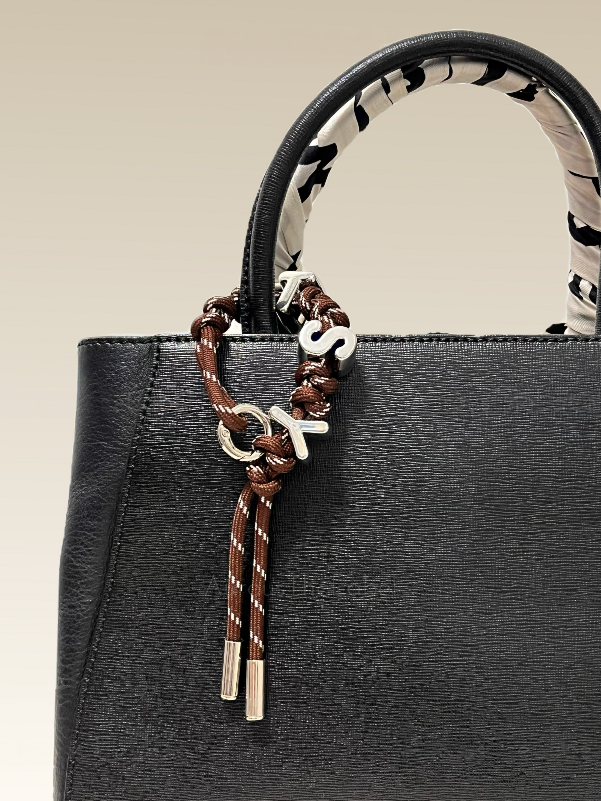 Black handbag with a decorative custom name keychain on a beige background