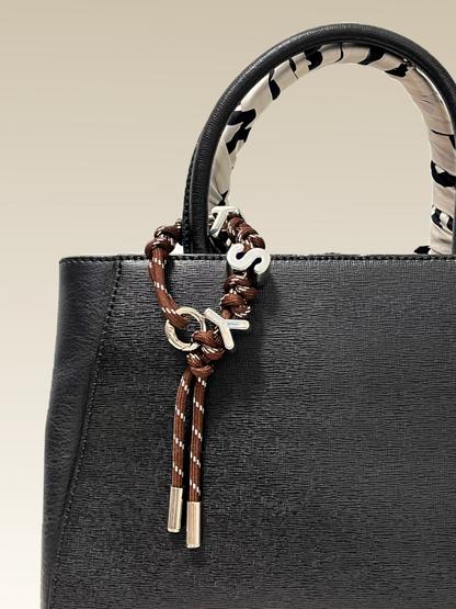 Black handbag with a decorative custom name keychain on a beige background