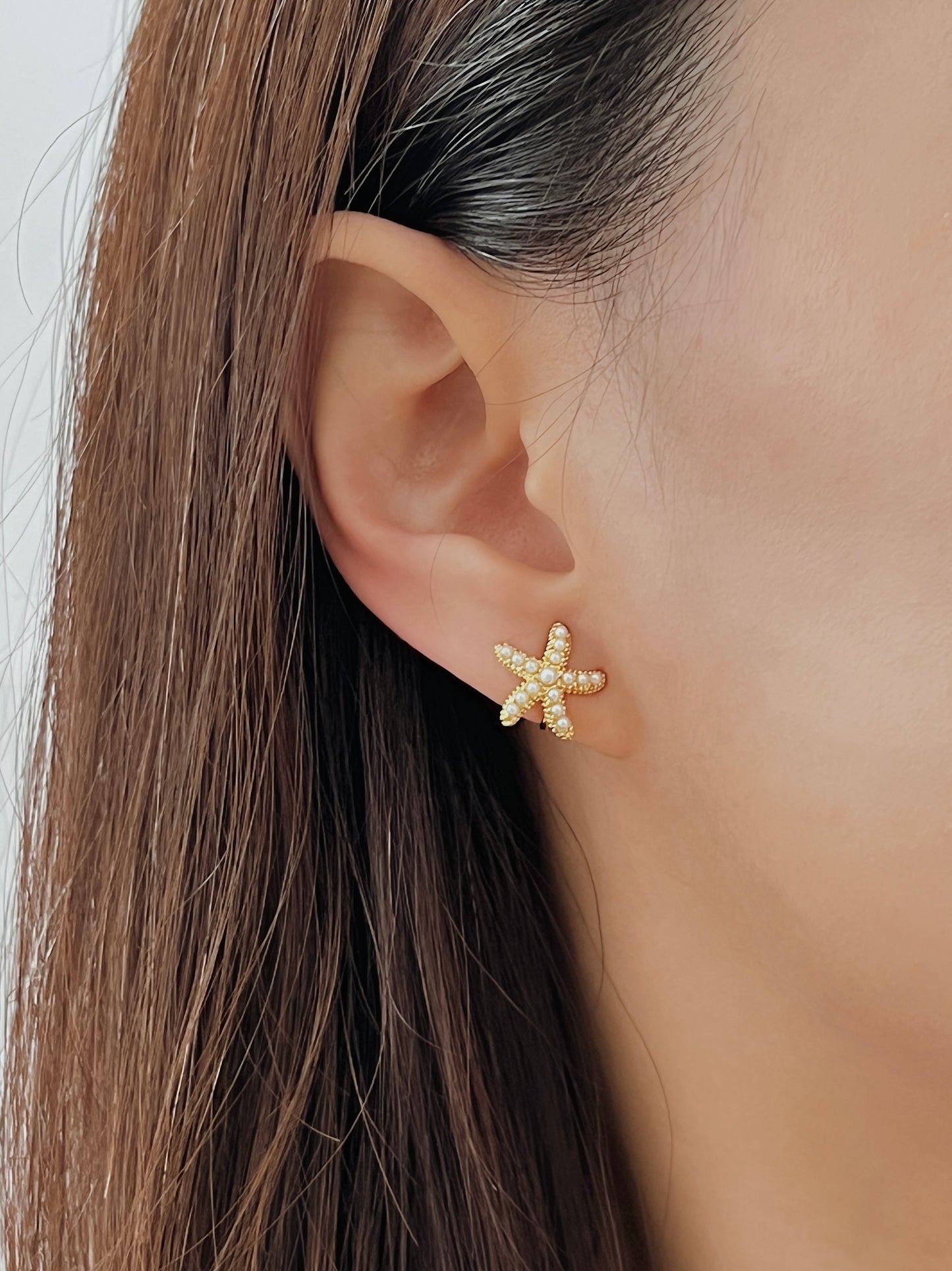 Gold starfish earring worn by a person with brown hair.