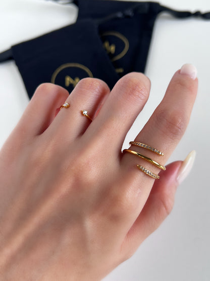 Hand wearing gold rings with a brand logo in the background