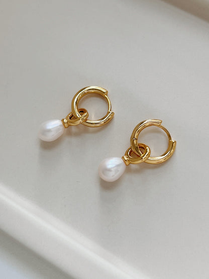 A pair of gold dangle pearl earrings placing on top of a beige tray plate.