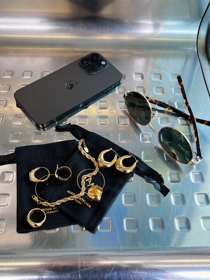 Flat lay of everyday essentials featuring aurous atelier gold jewelry, amalfi sunglasses and iphone.