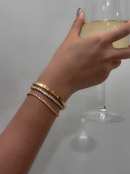 Gold tennis bracelet featuring diamonds on woman's wrist.