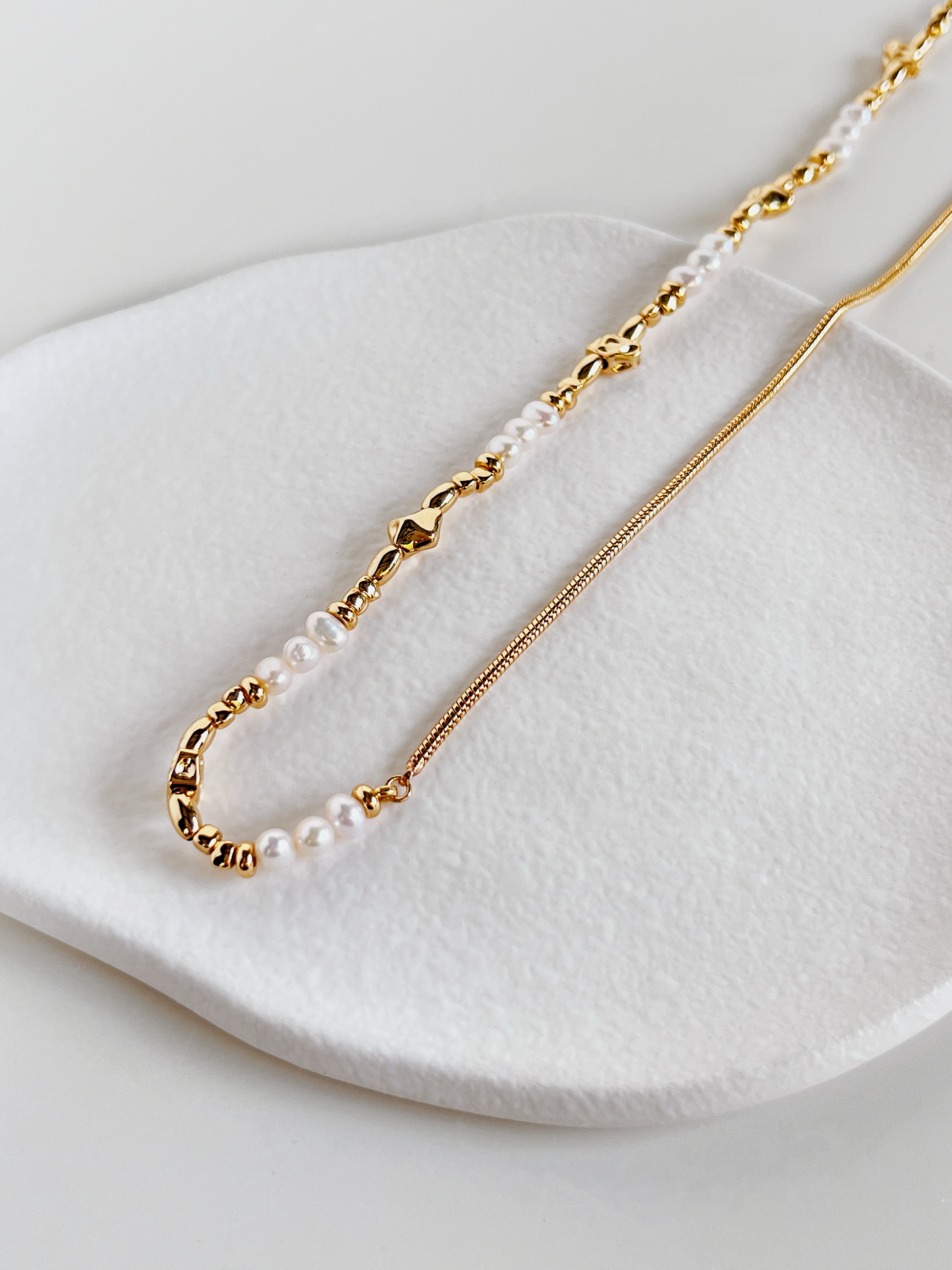 The Greta asymmetric half pearl half chain necklace displayed vertically against a clean white backdrop to illustrate its fluid chain drape.