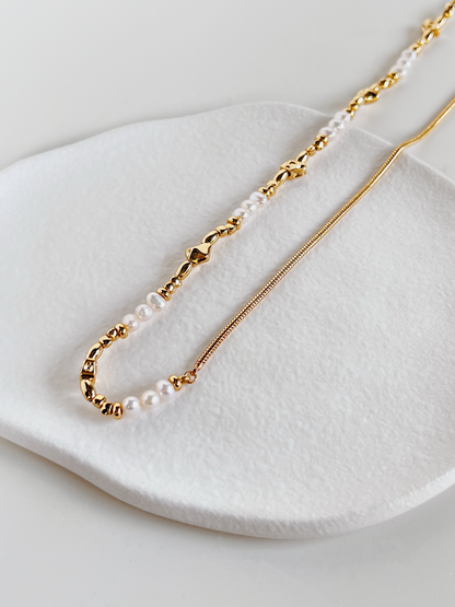The Greta asymmetric half pearl half chain necklace displayed vertically against a clean white backdrop to illustrate its fluid chain drape.