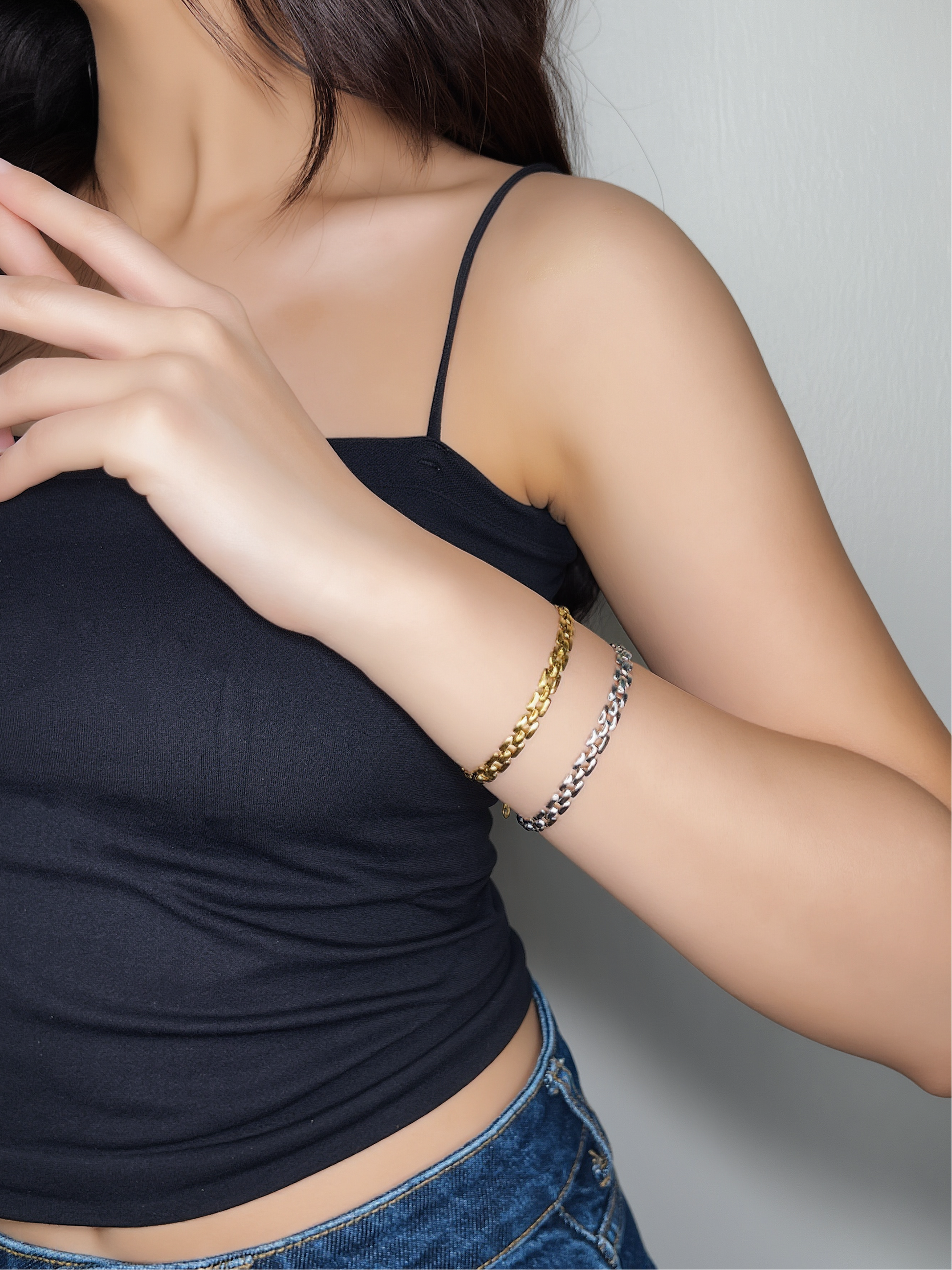 Person wearing a black top and blue jeans with gold and silver bracelet on her wrist on a neutral background