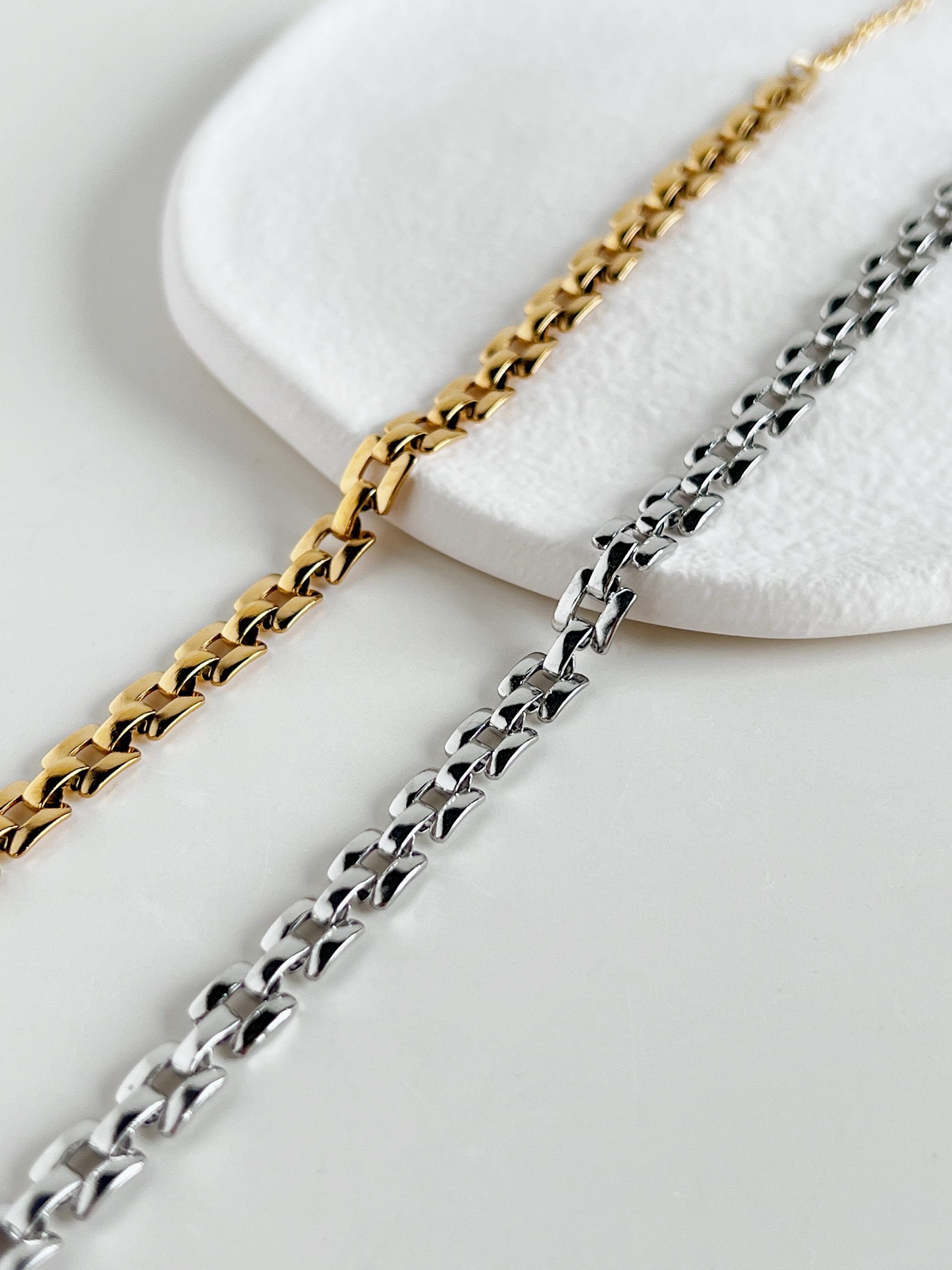 Two chain necklaces, one gold and one silver, on a white stone surface.
