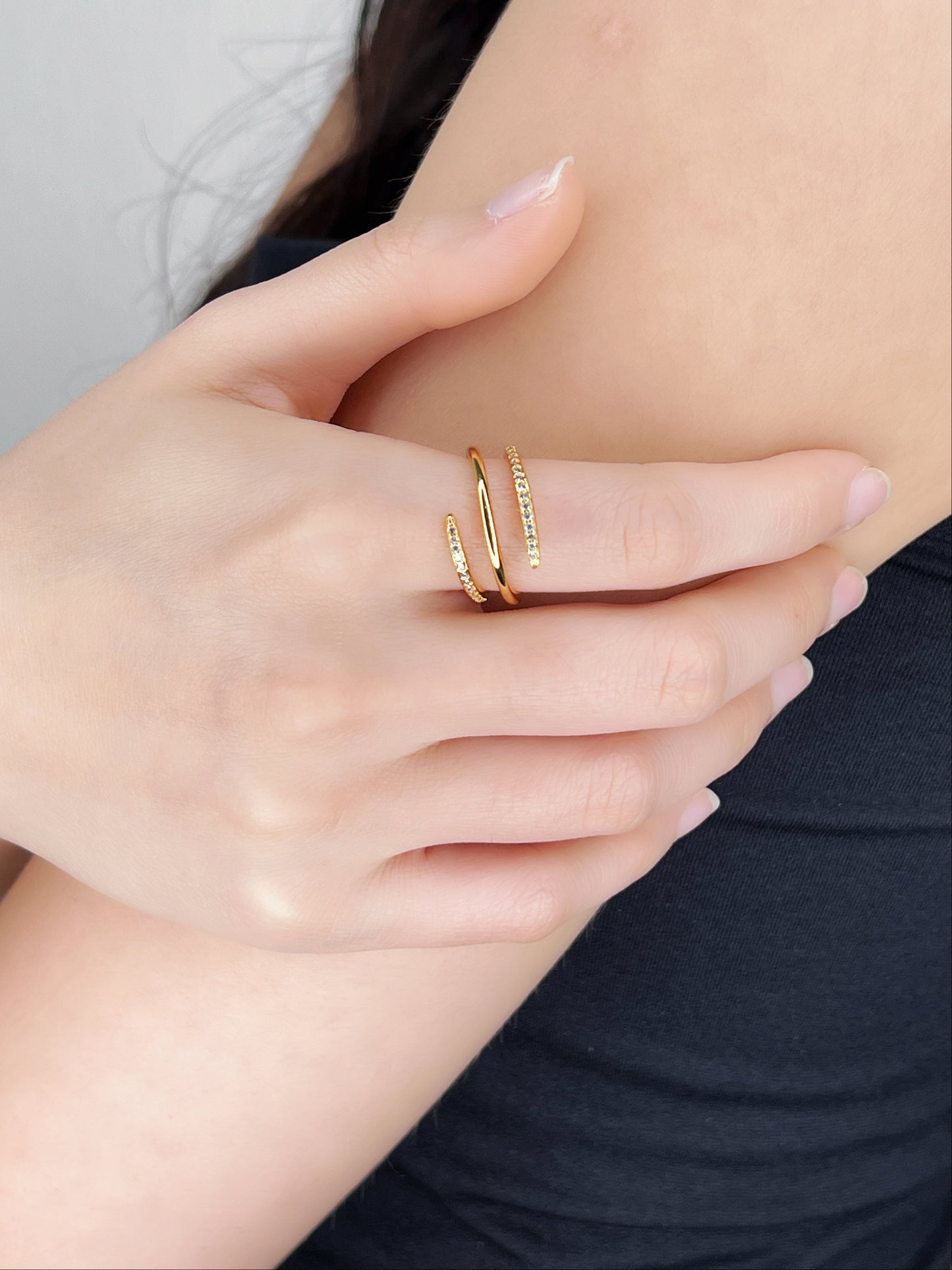 Close-up of a hand wearing gold spiral ring with gemstones with a blurred background