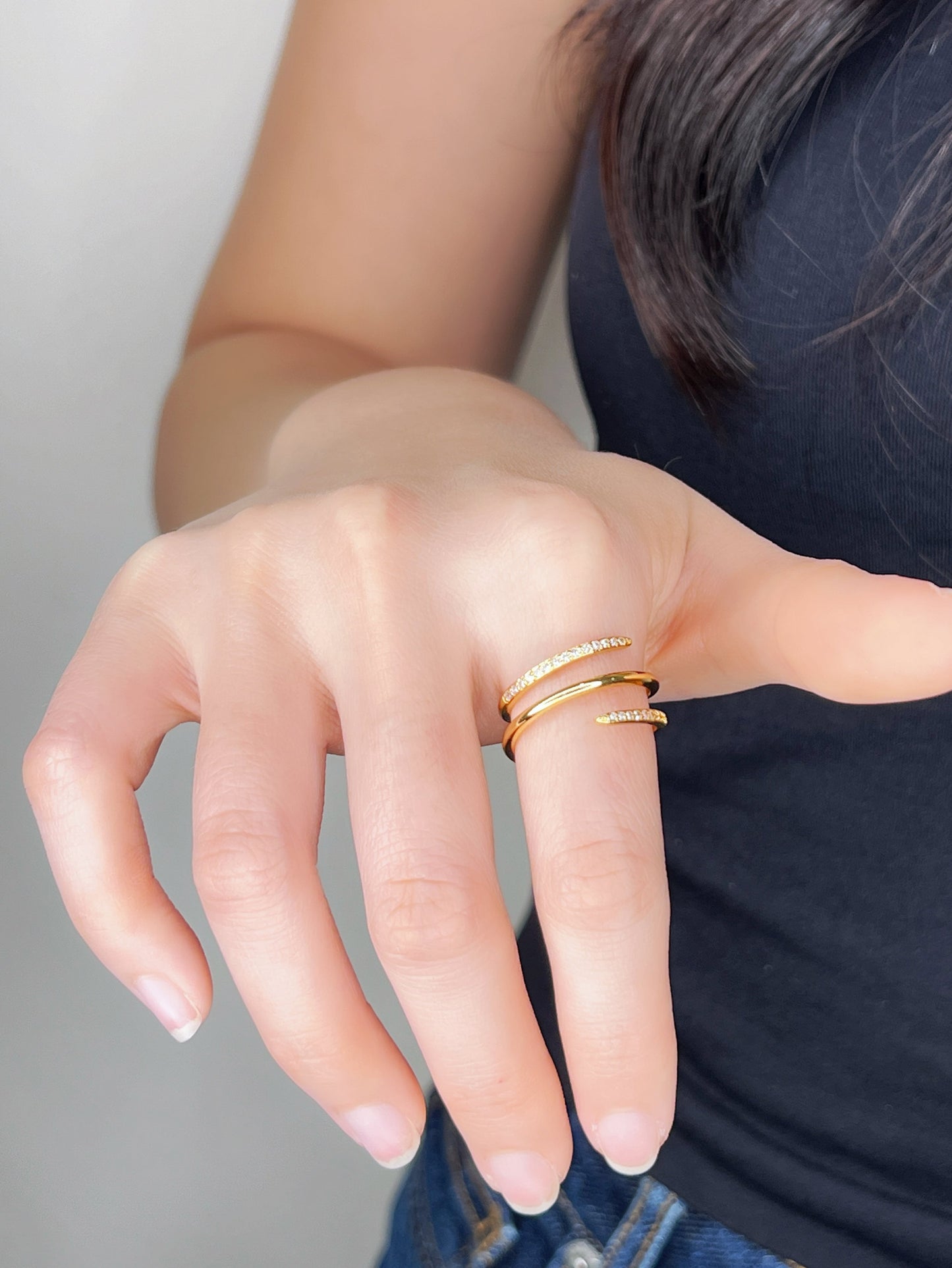 Hand wearing spiral gold rings on a neutral background