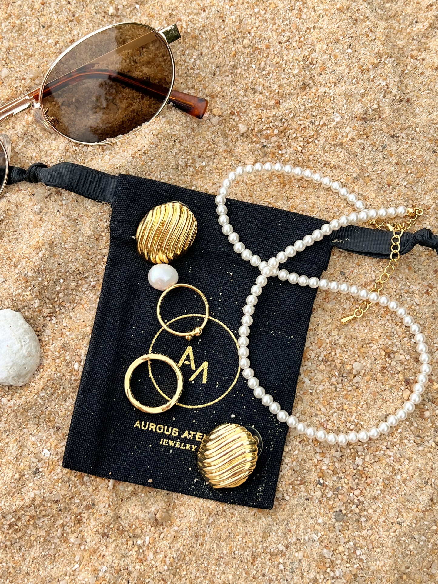 Durable moisture resistant fashion jewellery micro pearl chain and gold ribbed earrings resting on black jewellery pouch on the beach
