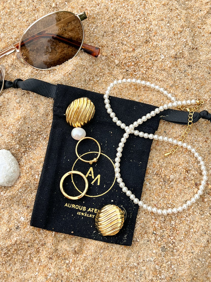 Durable moisture resistant fashion jewellery micro pearl chain and gold ribbed earrings resting on black jewellery pouch on the beach