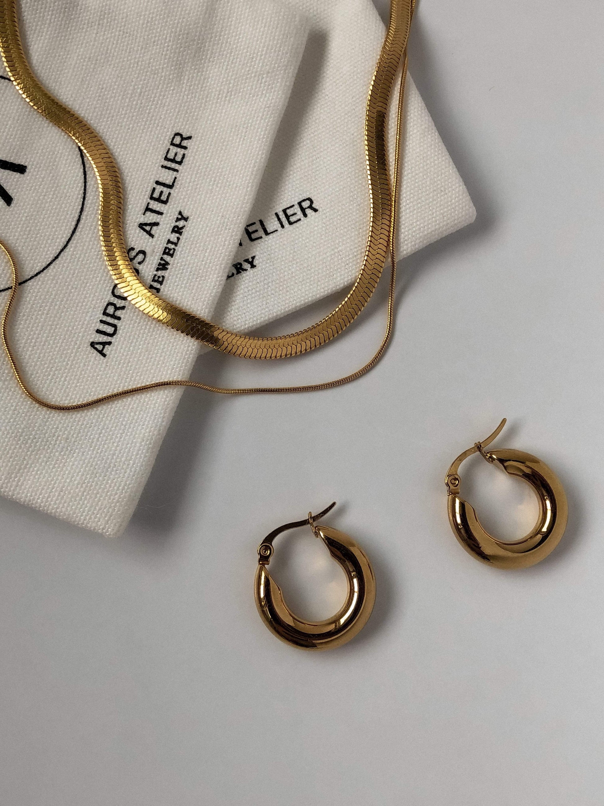 a flatlay image of a double layered gold herringbone and a pair of classic hoops on a white surface.
