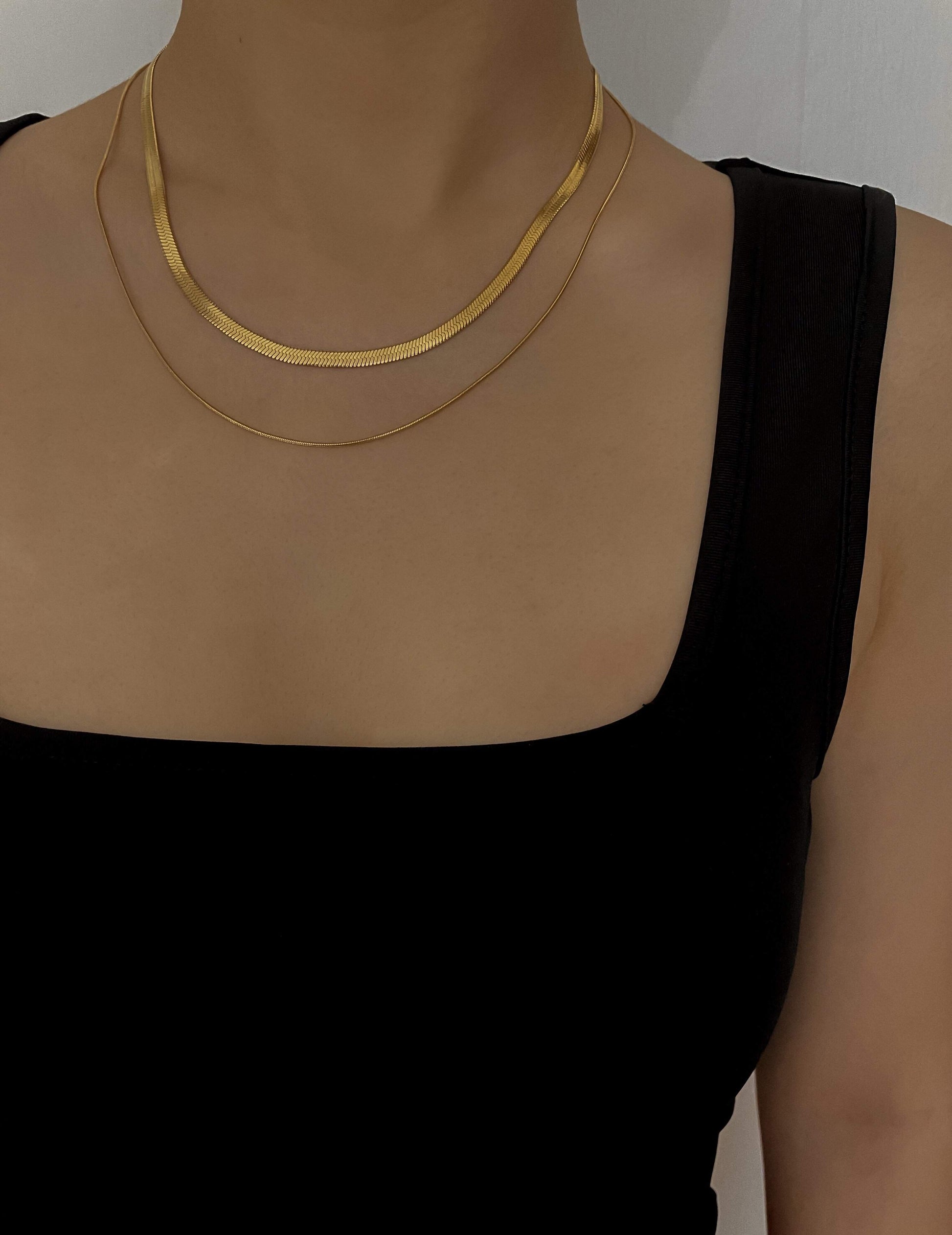 a woman wearing a gold layering necklace in 2 layers - featuring flat herringbone chain and thin snake chain.