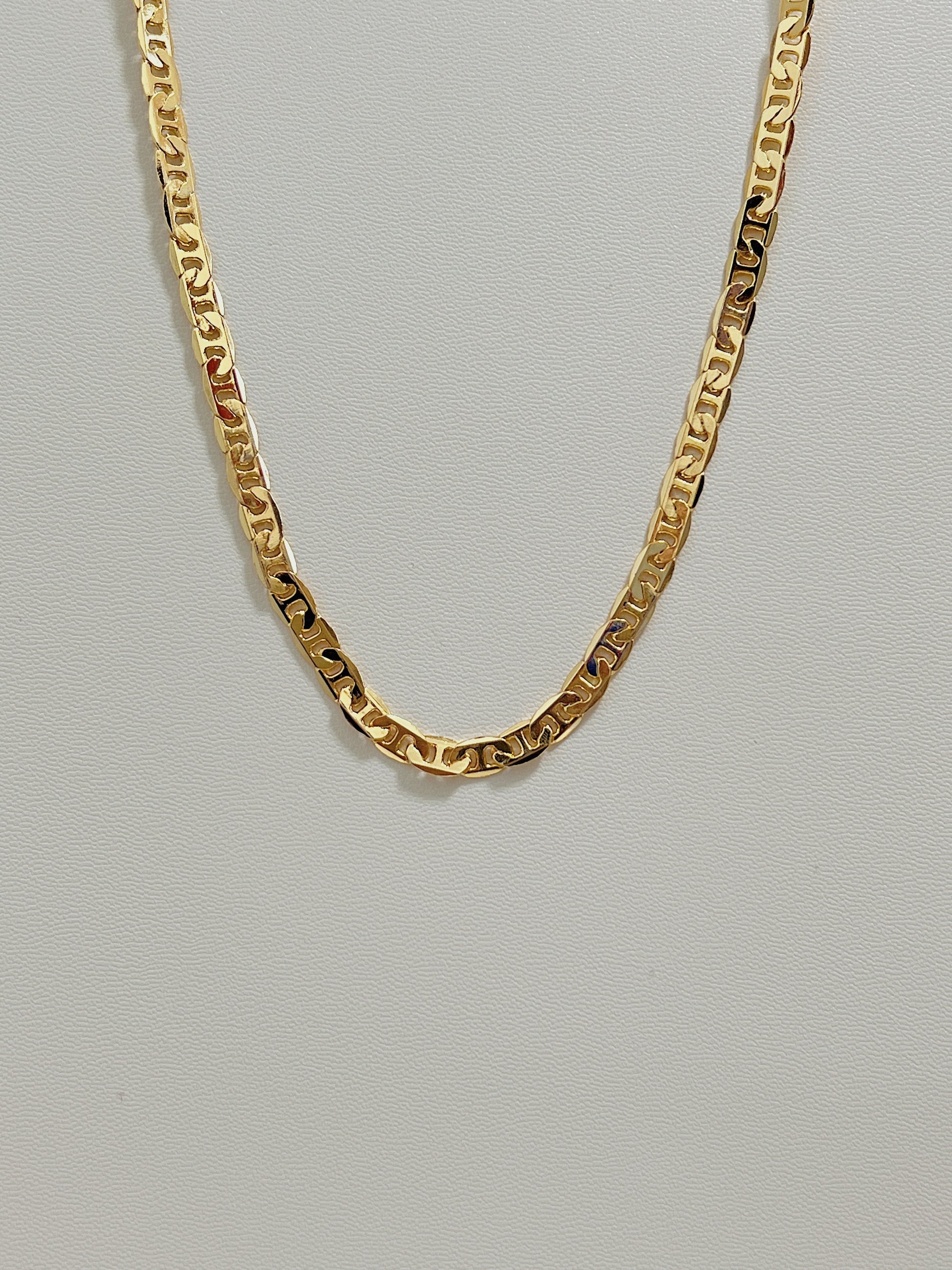 Studio view of the Alba mariner chain necklace showing its flat 4mm gold geometric link profile on a white leather background