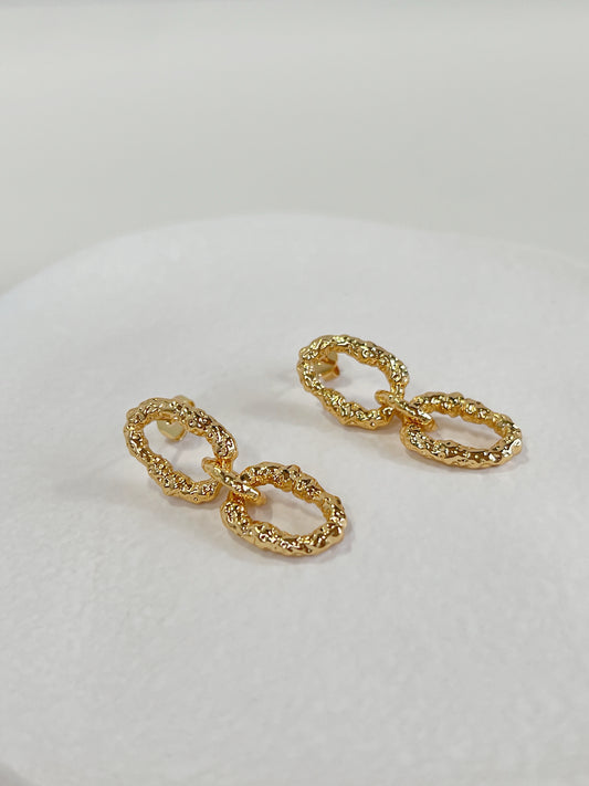 Studio product shot of a pair of gold alia molten metal link earrings on a clean white surface