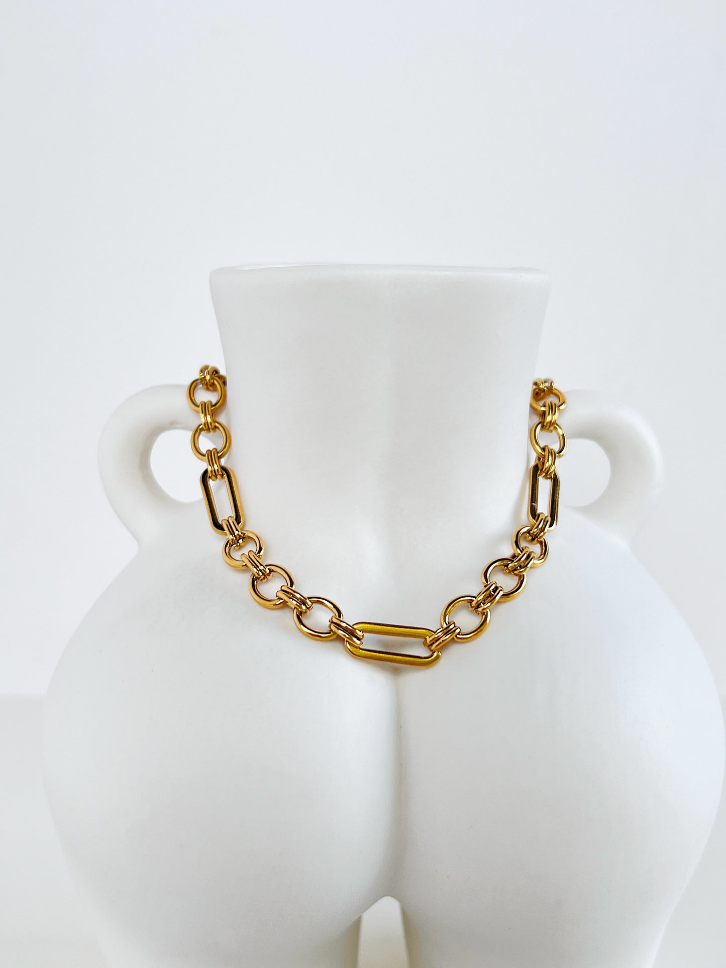 Macro detailed product shot of the Alyssa 18k gold PVD chain showcasing the polished straight bars and circular orbit rings on a minimalist white ceramic torso sculpture