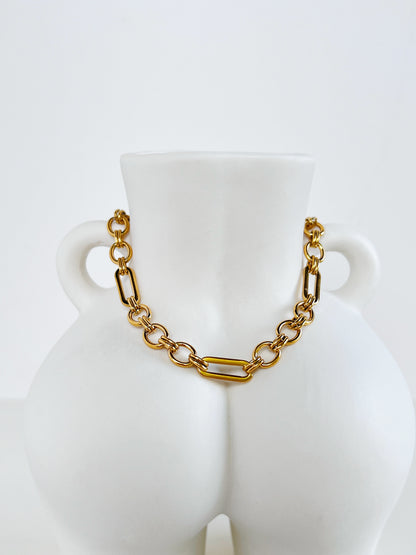 Macro detailed product shot of the Alyssa 18k gold PVD chain showcasing the polished straight bars and circular orbit rings on a minimalist white ceramic torso sculpture