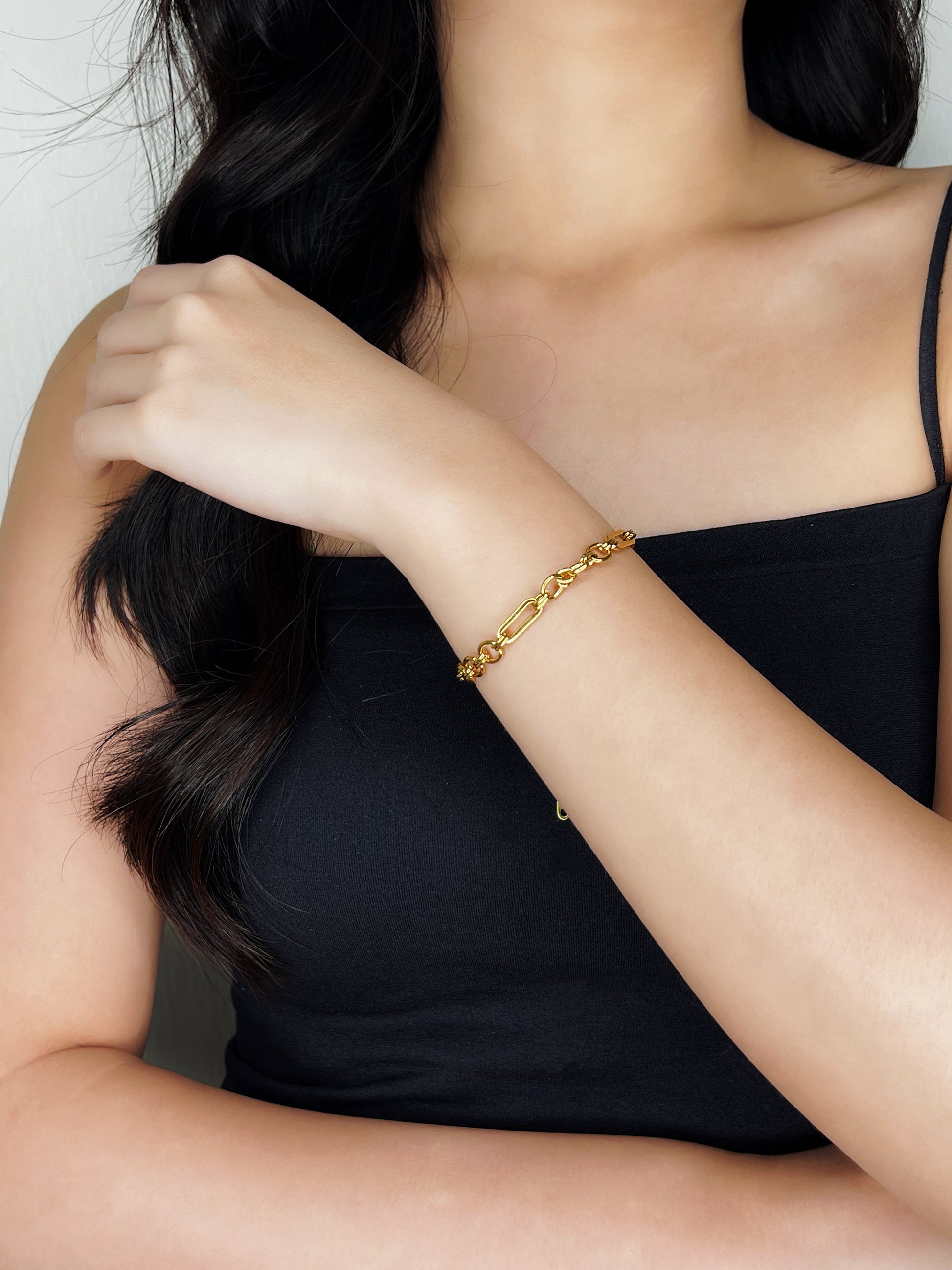 A model wearing the Alyssa mixed link chain bracelet on her wrist with her arm resting diagonally across her chest over a black tube top.