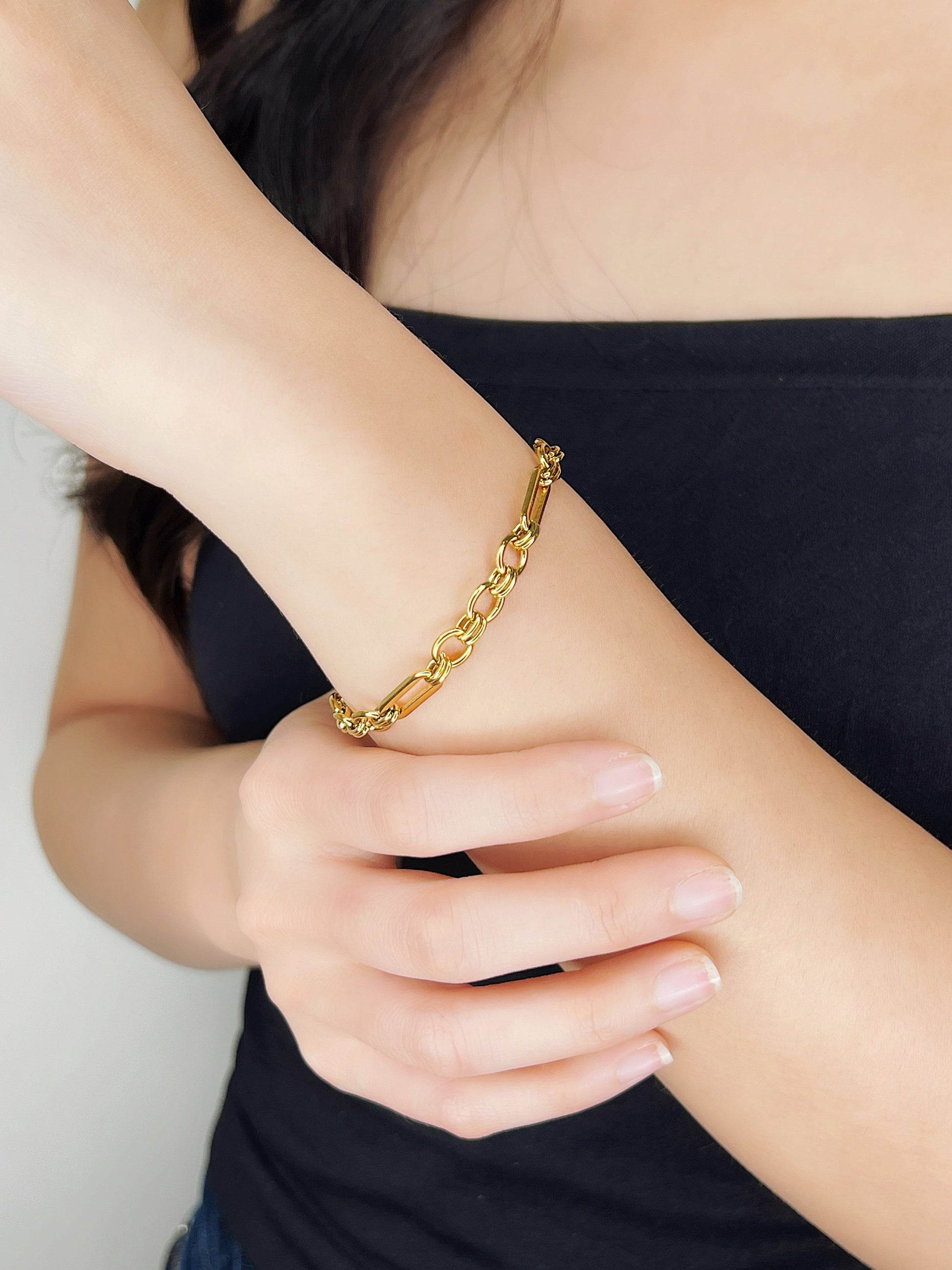 Mid-range lifestyle image of a model with her long dark hair, showcasing the golden shimmer of the Alyssa mixed link chain on her wrist