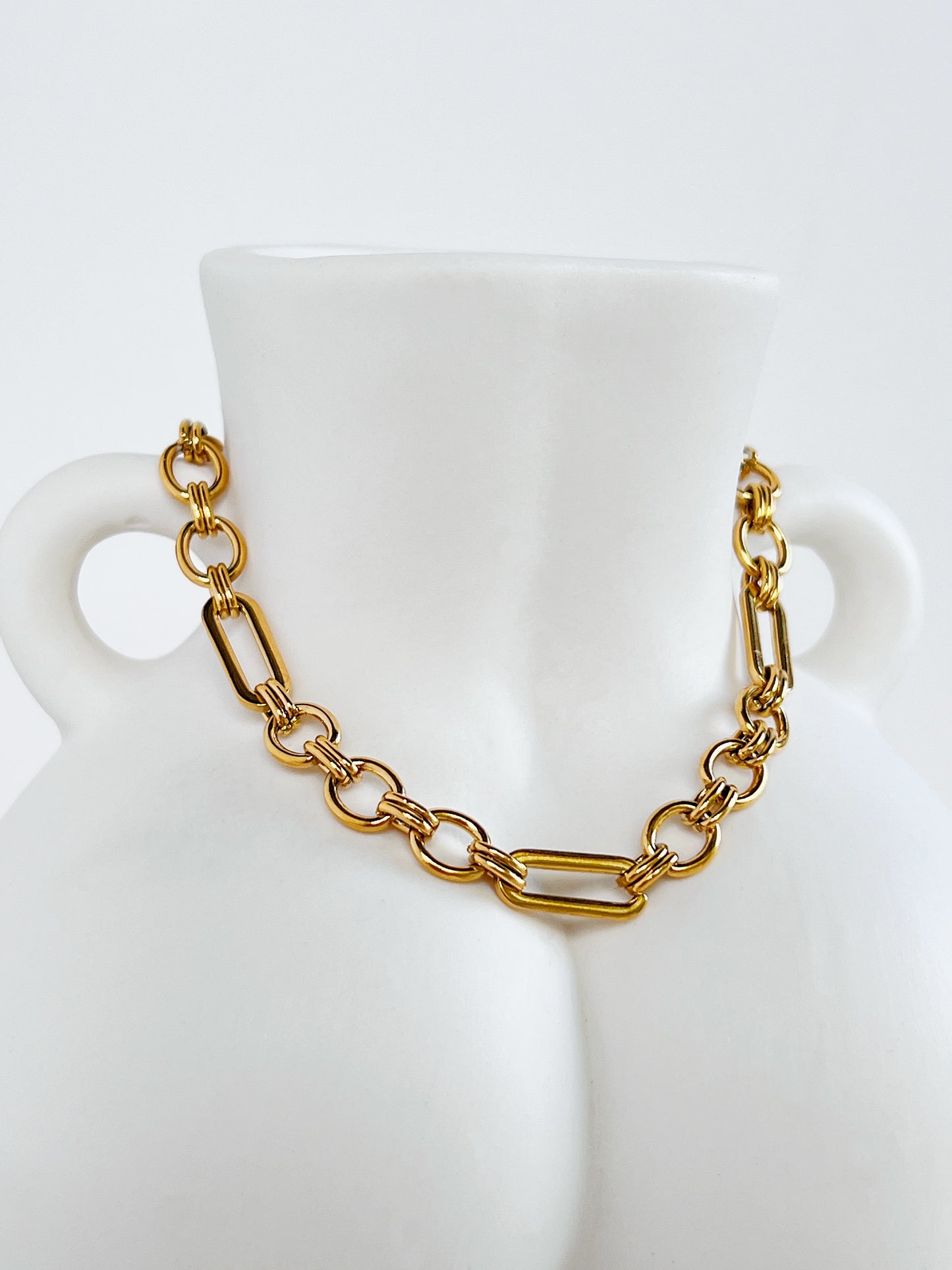 Close-up view of the Alyssa mixed link chain bracelet draped over the front curves of a white ceramic female bust vase, highlighting the alternating geometric links.