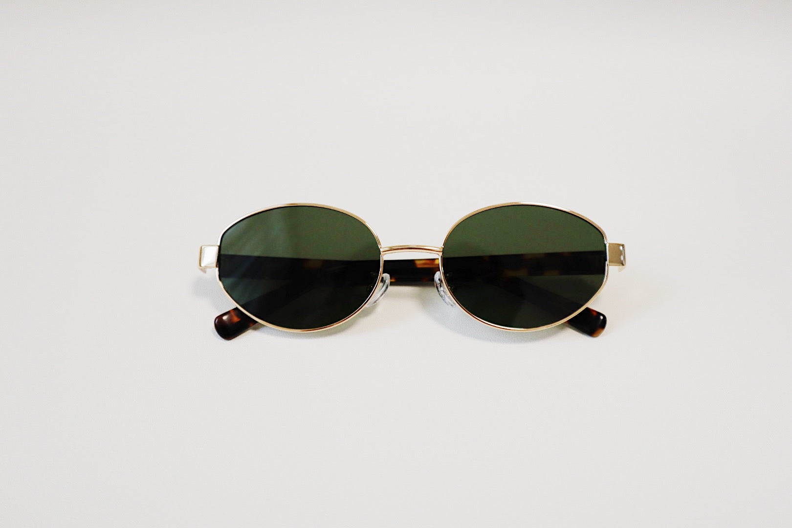 The Amalfi sunglasses folded flat on a stone display tray, showcasing the thick tortoiseshell panels and low-profile layout.