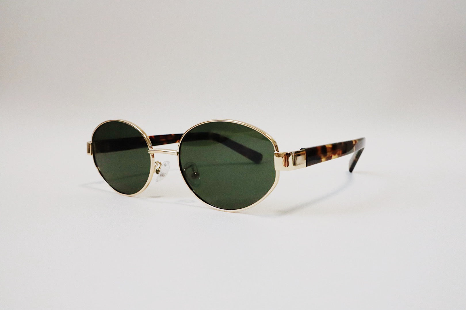 High-end product photography of Amalfi gold wire sunglasses resting on a minimalist surface, capturing the sharp contrast between the gold rim and deep green lenses.