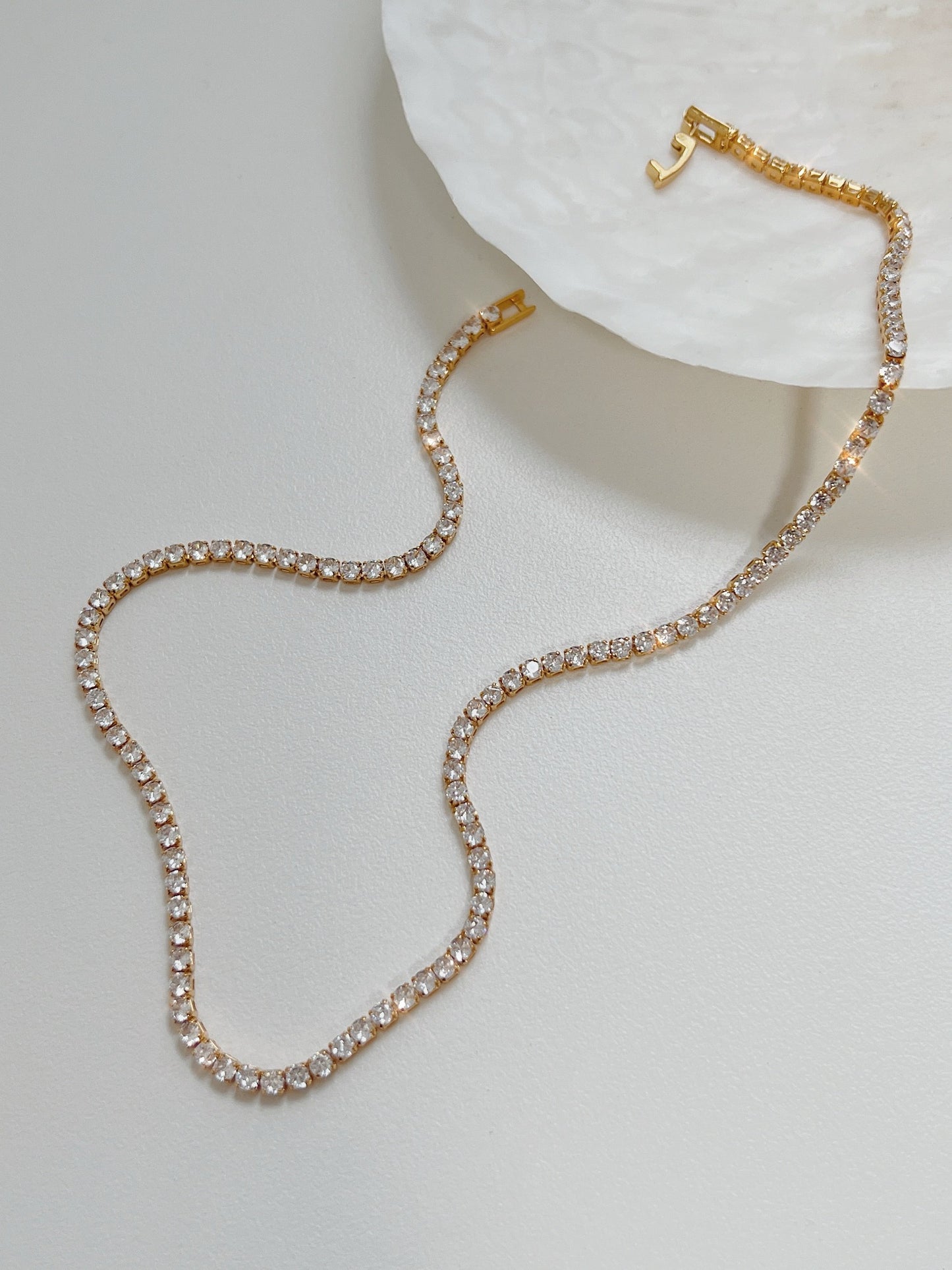 Amelia gold tennis necklace displaying single strand clear cubic zirconia stones on white surface
