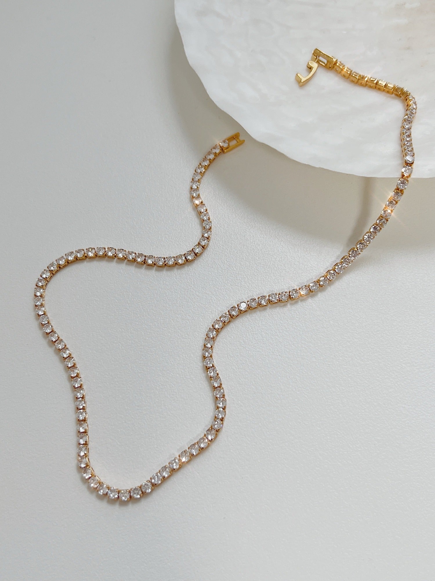 Amelia gold tennis necklace displaying single strand clear cubic zirconia stones on white surface