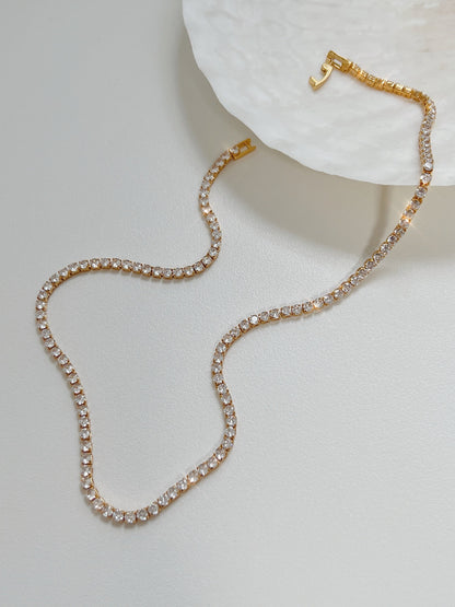 Amelia gold tennis necklace displaying single strand clear cubic zirconia stones on white surface