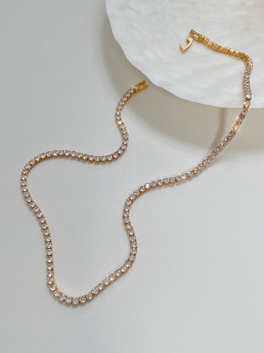 Amelia gold tennis necklace displaying single strand clear cubic zirconia stones on white surface