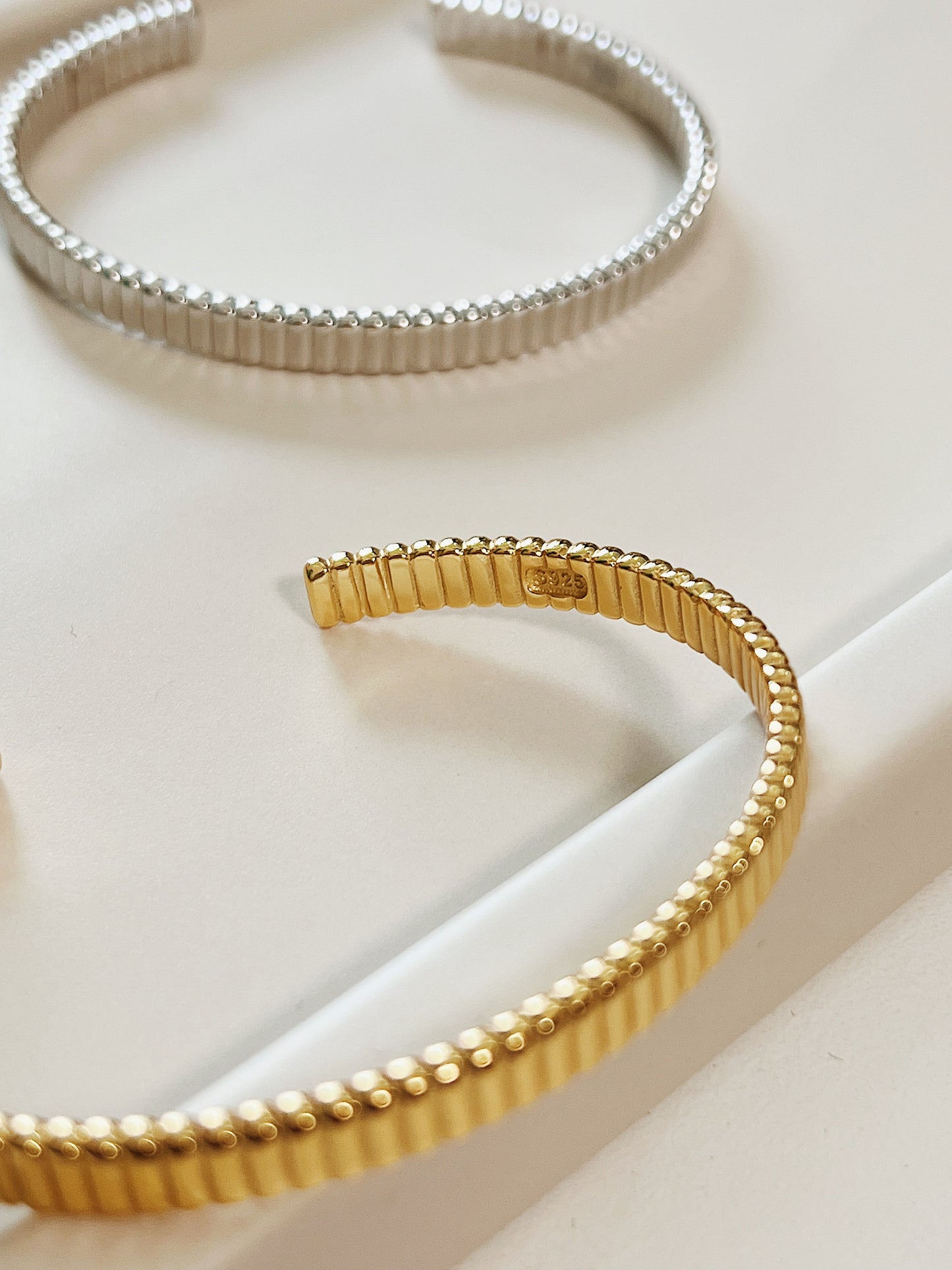 Angled presentation of the 18K gold vermeil ribbed flexible cuff bracelet resting solo to capture the reflective depth of its vertical ridges.