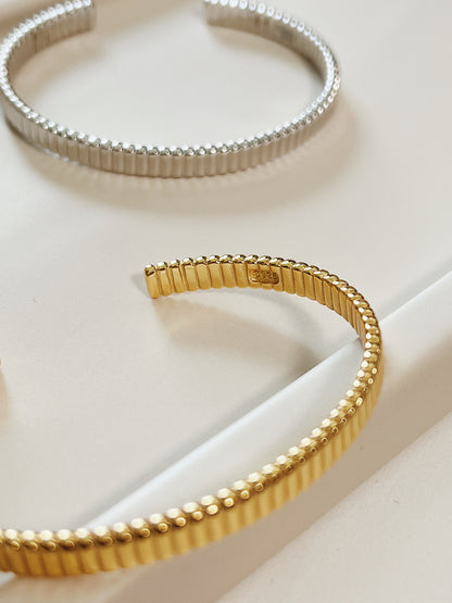 Angled presentation of the 18K gold vermeil ribbed flexible cuff bracelet resting solo to capture the reflective depth of its vertical ridges.