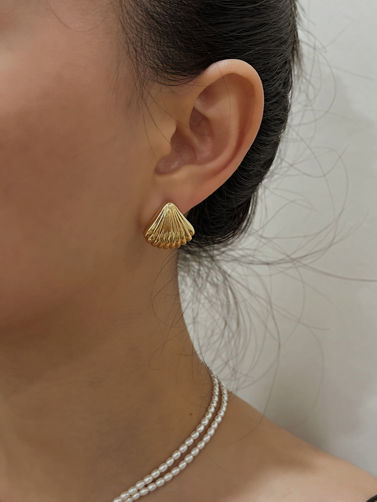 Model wearing Ariel gold shell clip-on stud earrings and pearl necklace