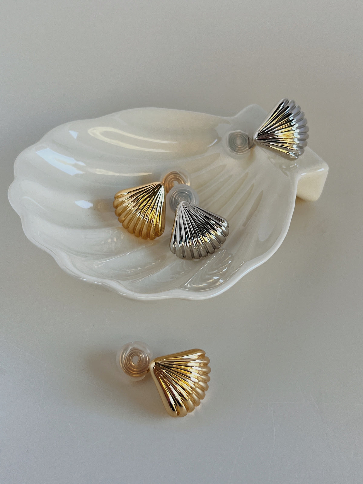 Ambient light reflecting off fluted scalloped architecture of Ariel gold and silver shell clip-on earring