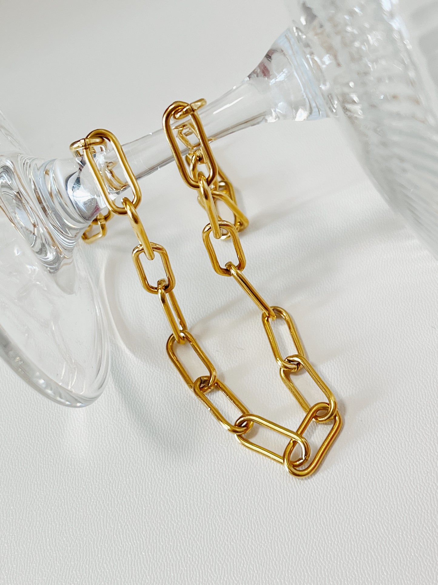 Structural view of Asher gold paperclip chain wrapped around the stem of an inverted crystal glass, showcasing how the links fluidly catch light.