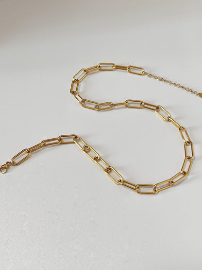 Close-up product photography of Asher chunky gold link necklace laid out in a fluid S-curve silhouette on a clean white surface, highlighting the geometric paperclip link design.