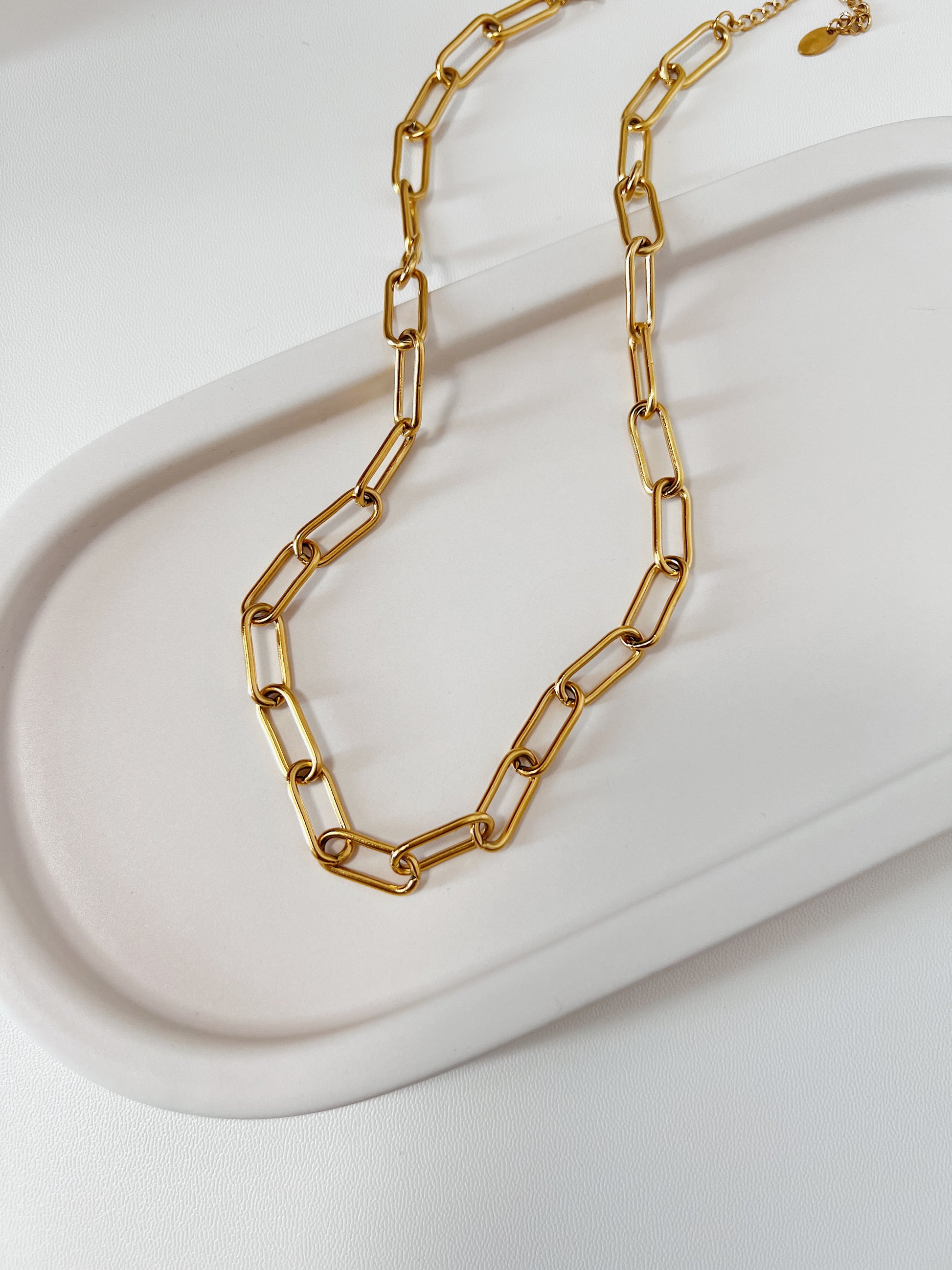 Textured product shot of Asher chunky link necklace resting on a ceramic plate surface, focusing on the seamless alignment and crisp edges of the metallic links.