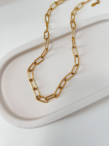 Textured product shot of Asher chunky link necklace resting on a ceramic plate surface, focusing on the seamless alignment and crisp edges of the metallic links.