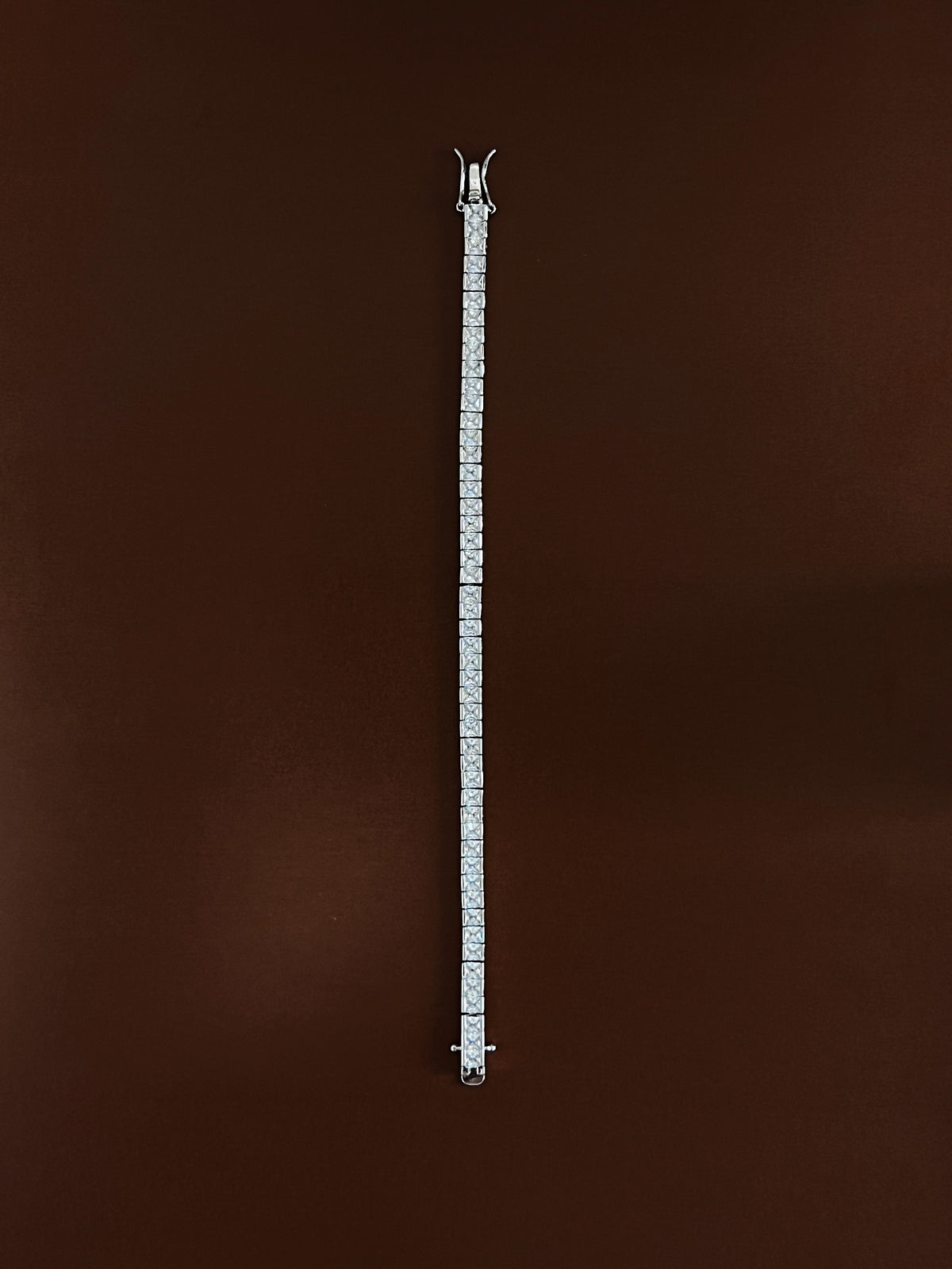Full-length overhead view of the silver Astra channel set tennis bracelet featuring 3mm square princess-cut stones laid straight on an espresso background to display total length and continuous sparkle for capsule wardrobe jewelry stacks.